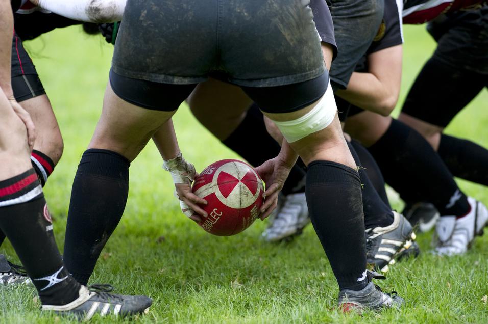 Rugby-Spieler in kniender Position, die einen roten Rugbyball im Gras vorbereiten.